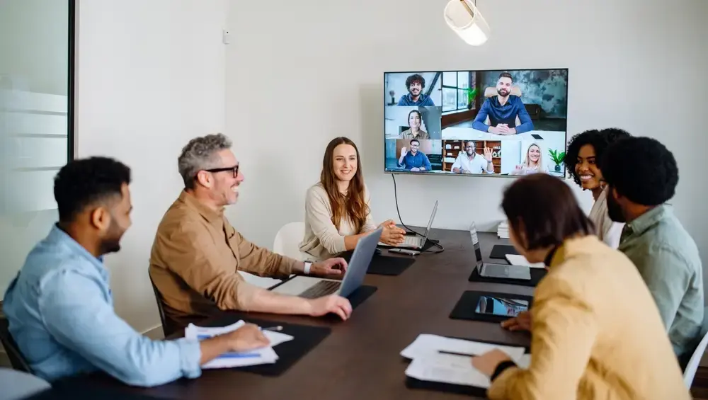 A group in a conference room with a networked call on screen